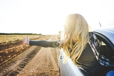 Young woman with arms outstretched leaning out from car window against clear sky