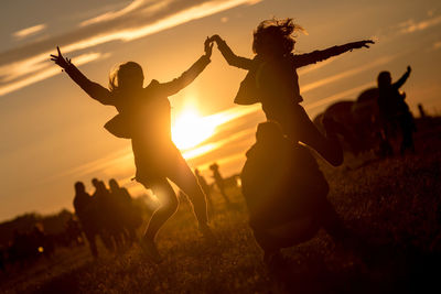 Female friends jumping while man crouching at park during sunset