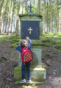 Rear view of boy standing by tree in forest