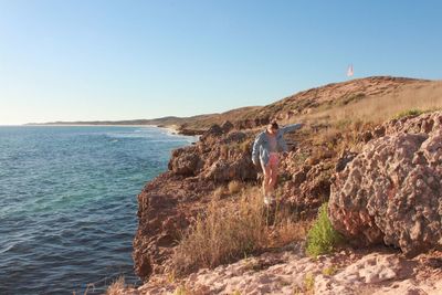 Woman standing on rock by sea against clear sky