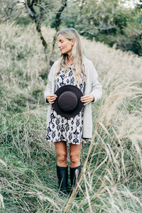 Beautiful pregnant woman stands in the park in autumn and covers her belly with a hat