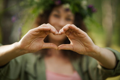 Smiling middle-aged caucasian woman making heart with hands in summer forest