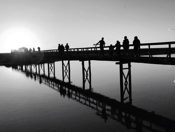 Silhouette people on footbridge over river against clear sky