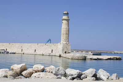 Lighthouse by sea against clear sky