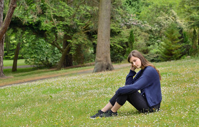 Portrait of girl sitting on grassy field against trees