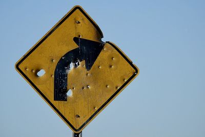 A yellow street sign indicating a curve in the road ahead is riddled with bullet holes.