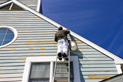 Low angle view of man painting house while standing on ladder