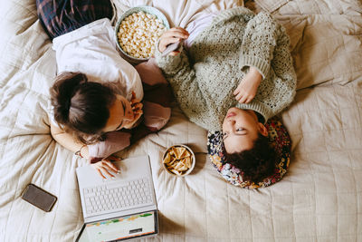 Directly above shot of female friends talking while lying on bed at home