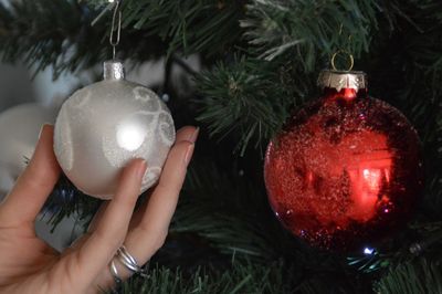 Close-up of hand holding bauble hanging from christmas tree