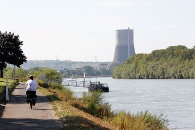 Woman cycling on riverbank against sky