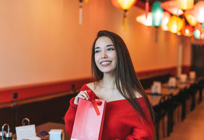 Beautiful young asian woman in red clothes with red gift bag in restaurant chinese new year