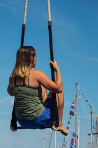 Low angle view of boy on swing against clear blue sky