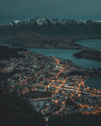 High angle view of illuminated cityscape by lake against mountains at night