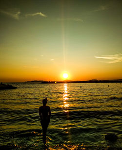 Rear view of silhouette man standing in sea against sky during sunset