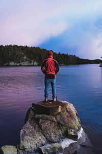 Rear view of man standing on rock by lake against sky