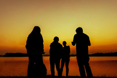 Silhouette people looking at lake against orange sky