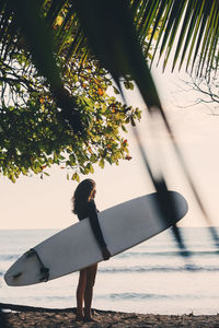 Full length side view of mature woman carrying surfboard at beach