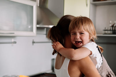 Mother carrying crying daughter at home