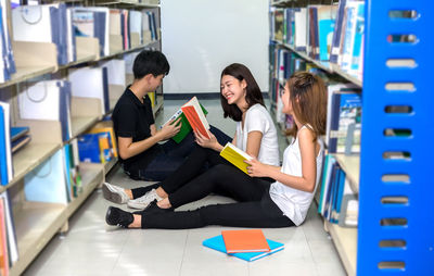 High angle view of happy friends studying while sitting on floor in library