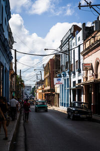 Cars on city street by buildings against sky