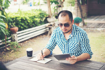 Man with disposable cup using digital tablet outdoors