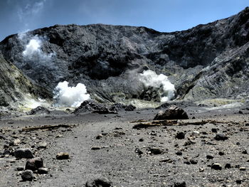 Steam at volcanic landscape against cloudy sky