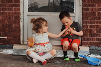 Siblings sitting on doorway against brick wall