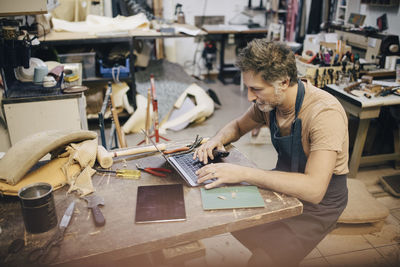 Male craftsperson using laptop at workbench in workshop