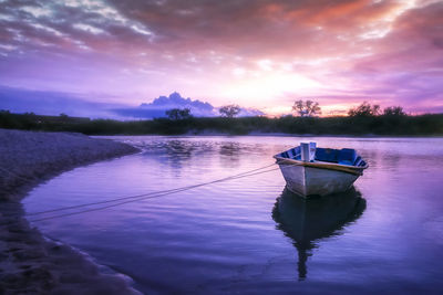 Boat moored in lake against sky during sunset