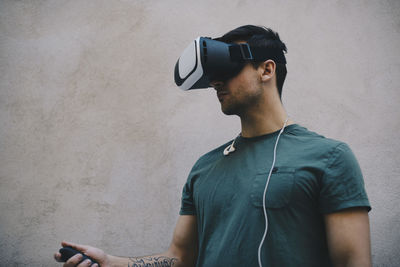 Computer programmer using vr glasses and remote control against beige wall in office