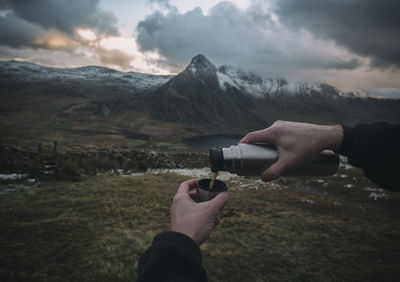 Close-up of hand holding water against mountain range