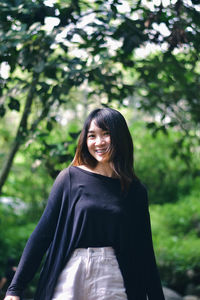 Portrait of young woman standing against trees