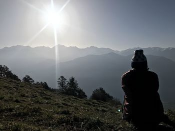 Rear view of man sitting on mountain against sky