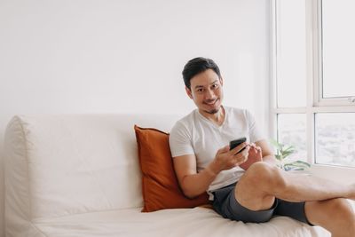 Smiling man with smart phone sitting on sofa at home