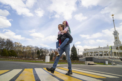 Smiling man giving piggyback ride to girlfriend on zebra crossing