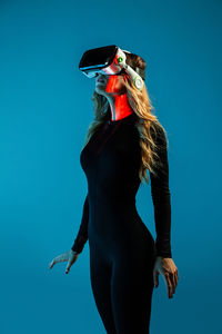 Young woman looking away while standing against blue background