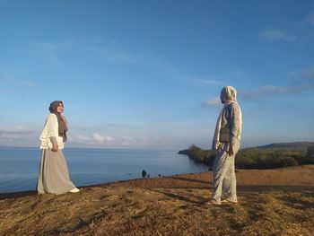 Rear view of people standing by sea against sky