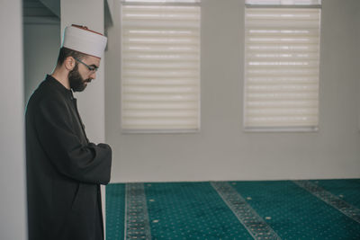 Side view of young man standing against wall