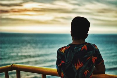 Rear view of man standing by sea during sunset