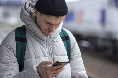 Man using smartphone, texting, cheks route of trip on google mapes, waiting train at railway station