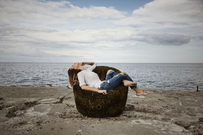 Woman sitting on beach by sea against sky