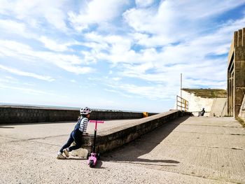 Rear view of child with push scooter on road during sunny day