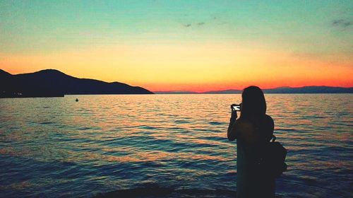 Man photographing sea against sky during sunset