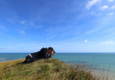 Rear view of woman sitting on cliff by sea against sky