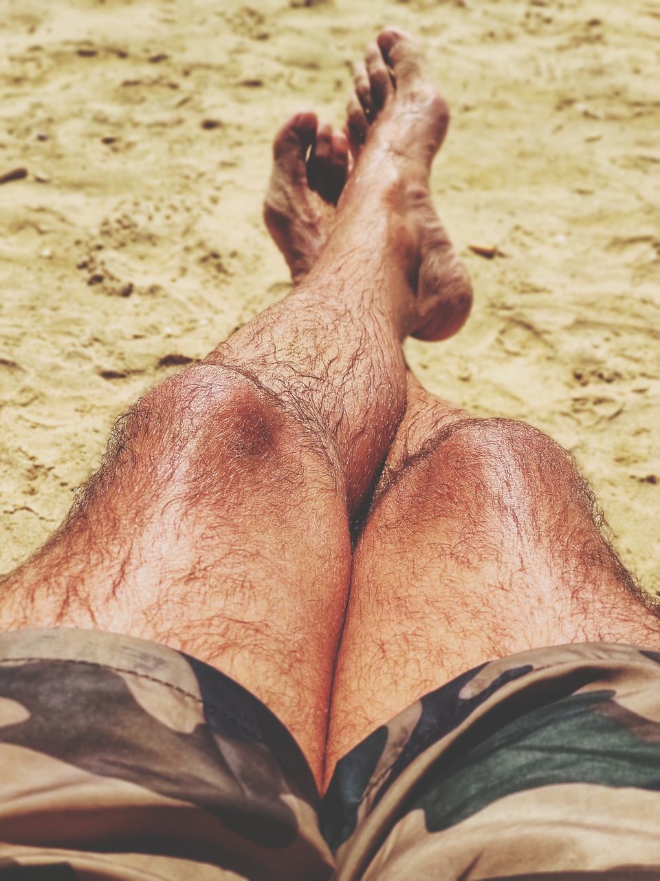 LOW SECTION OF MAN LYING DOWN ON SAND