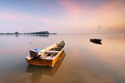 Boats moored on lake against sky during sunset