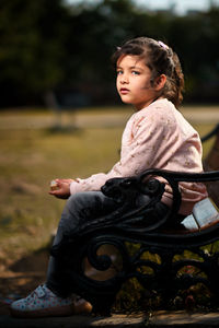 Portrait of young woman sitting on bench at park