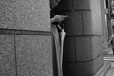 Side view of man holding mobile phone against wall