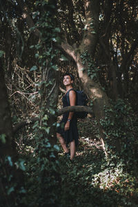 Portrait of young woman standing by tree trunk in forest