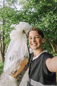 Portrait of happy teenage boy showing garbage bag